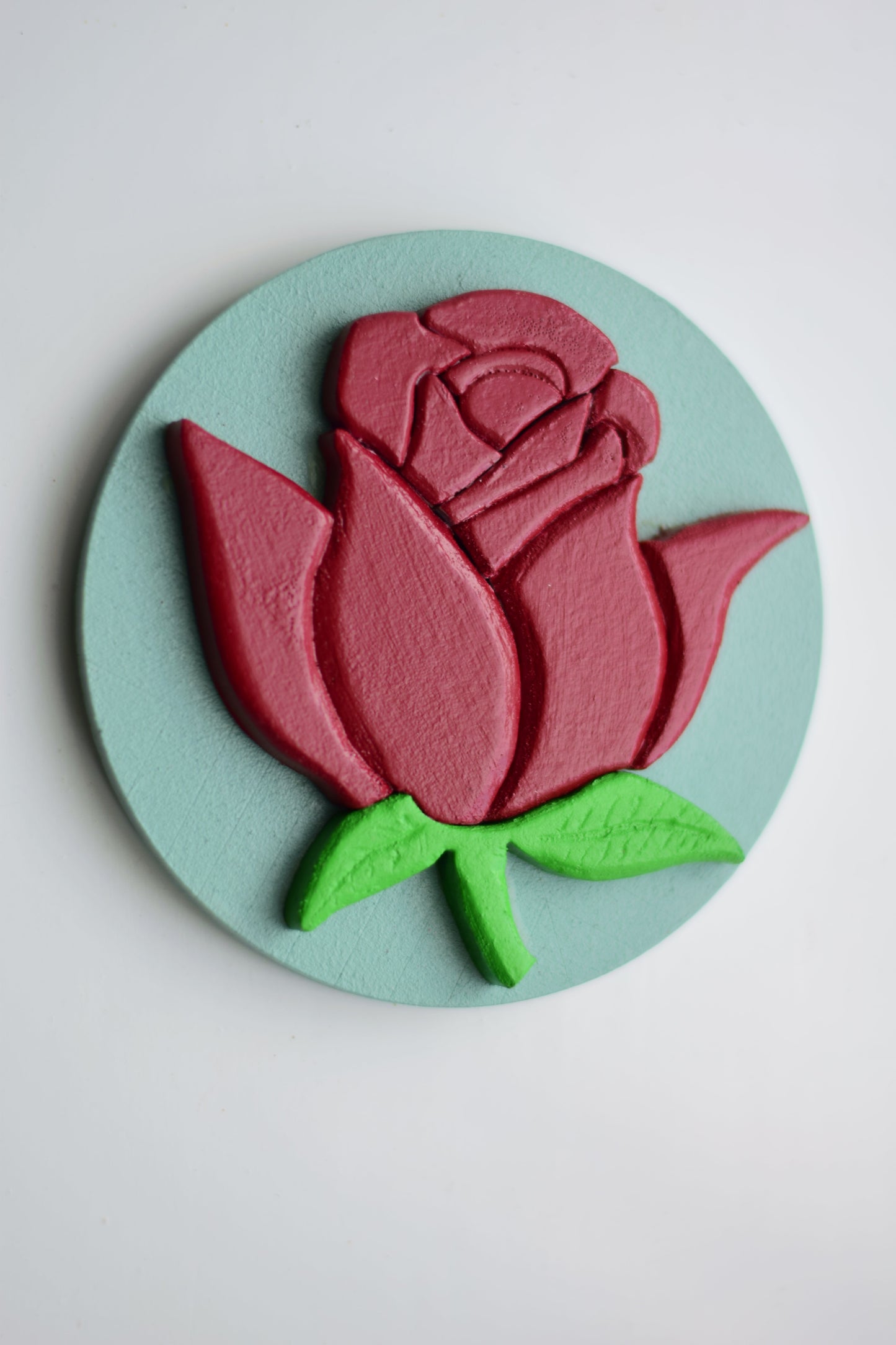 Decorative wall art with a red rose and green leaves on a light blue background
